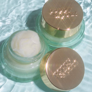 Two mint green glass jars of Poppy & Pout lip mask with gold lids, one open showing white balm inside.