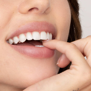Woman pointing to her white teeth while wearing natural pink lip tint and smiling.