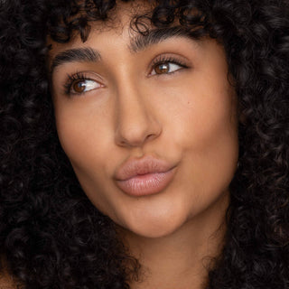Woman with curly hair wearing natural-looking lip tint, showcasing smooth, glossy lips and glowing skin.