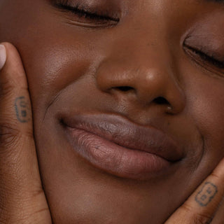 Close-up of person with closed eyes wearing natural lip tint, hands gently framing face