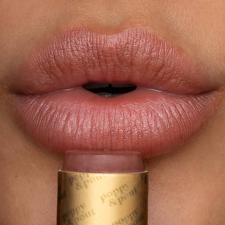Close-up of lips wearing natural pink lip tint with gold Poppy & Pout tube below