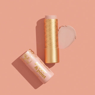Two lip balm tubes with gold and pink packaging displayed on a coral pink background with product swatches.