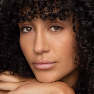 Woman with curly hair wearing natural-looking lip tint, showcasing healthy glowing skin and subtle makeup.