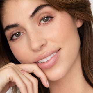 Woman with natural makeup smiling while touching her face, wearing pink lip tint.