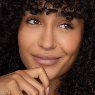 Woman with curly hair wearing natural-looking lip tint, smiling with hand near chin