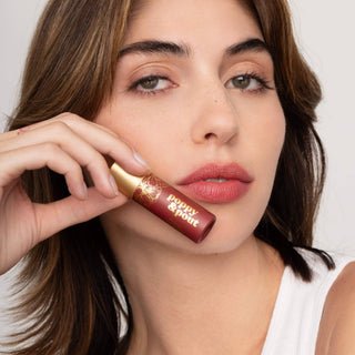 Woman holding Poppy & Pout lip tint tube while wearing matching coral-pink lip color