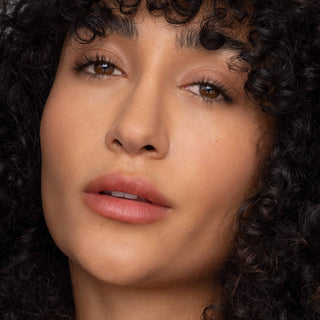 Woman with curly hair wearing natural-looking lip tint with subtle coral-pink color and glossy finish.