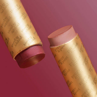 Two golden lip tint tubes with pink caps against a burgundy background, one open showing product inside.