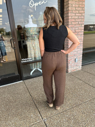 Woman wearing the Little Black Luxe Top paired with brown linen pants, rear view, outside boutique.