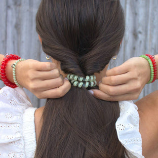 Woman styling brown hair with spiral hair tie, wearing colorful beaded bracelets