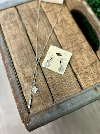 Silver clover pendant necklace and matching drop earrings set displayed on rustic wooden crate.