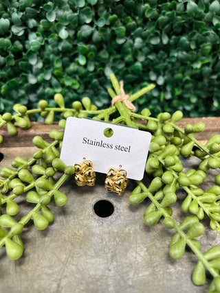 Gold-toned chain link hoop earrings on stainless steel card surrounded by green foliage on wooden surface.