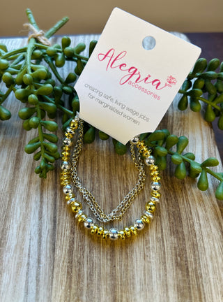 Gold and silver beaded bracelet with chain detail on wooden surface with succulent plant and brand tag.