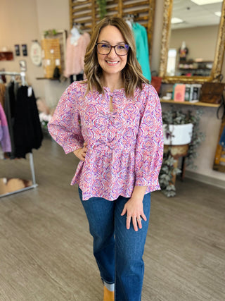 Woman wearing paisley patterned tie-front blouse with jeans in clothing boutique setting