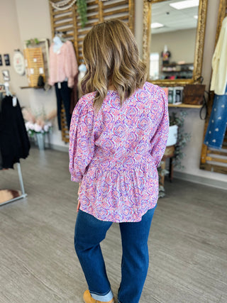 Woman wearing paisley patterned blouse and jeans, shown from behind in clothing boutique setting.
