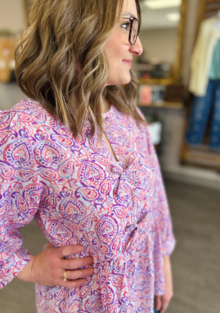 Woman wearing paisley patterned tie blouse with long sleeves, smiling in profile view indoors.