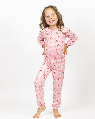 Young girl wearing pink holiday pajamas with vintage Santa print, smiling and posing against white background.