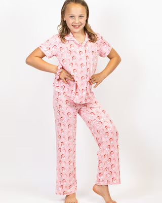Young girl wearing pink holiday pajama set with vintage Santa print, hands on hips, smiling.