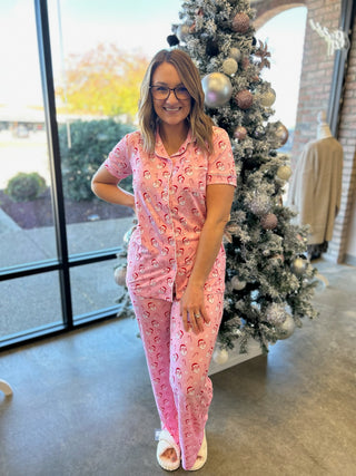 Woman wearing pink holiday pajamas with vintage Santa print standing beside decorated Christmas tree