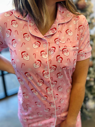 Woman wearing pink Christmas pajamas with Santa face and candy cane pattern, button-up top with collar.