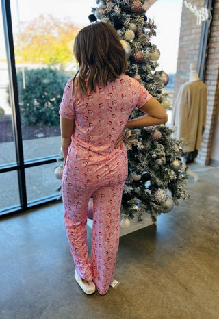 Woman wearing pink vintage Santa print holiday pajamas standing next to decorated Christmas tree
