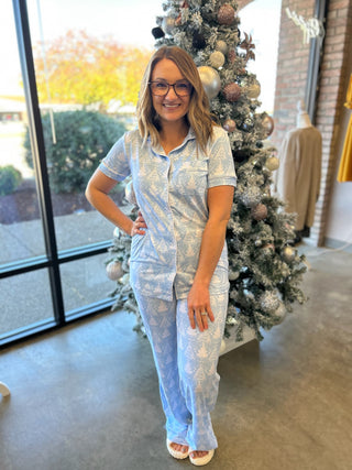 Woman wearing light blue patterned holiday pajama set posing next to decorated Christmas tree indoors