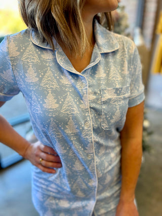 Woman wearing light blue holiday pajama top with white Christmas tree and snowflake pattern.