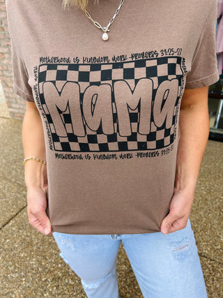 Woman wearing brown "MAMA" graphic t-shirt with checkered pattern and biblical text, paired with distressed jeans.