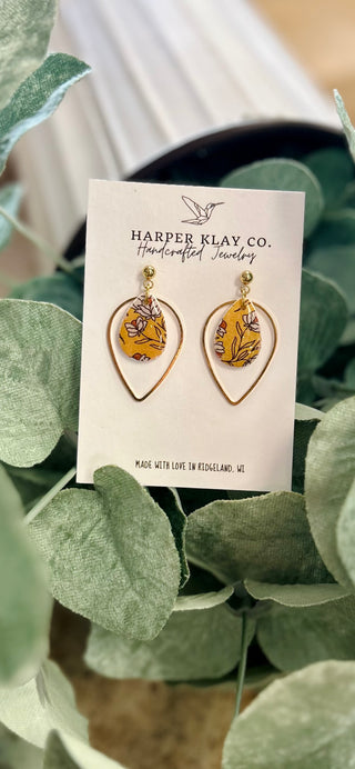 Handcrafted teardrop earrings with floral pattern displayed on branded card among green foliage