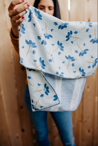 Woman holding white kitchen towel with blue floral pattern and gold stems against wooden background