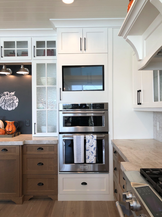 Kitchen towels hanging on stainless steel oven handle in modern farmhouse kitchen with white and wood cabinets.