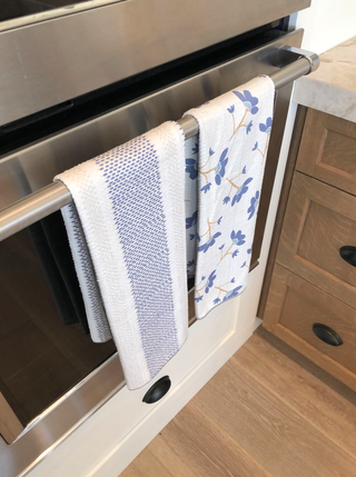 Kitchen towels hanging on oven handle, showing blue striped and floral patterns in modern kitchen setting.