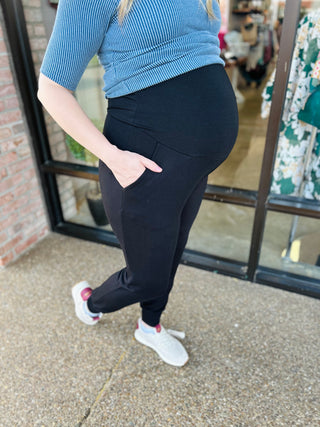 Pregnant woman wearing maternity knit jogger pants with high waistband and pockets, paired with striped top.