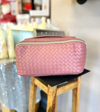 Woven leather makeup bag with zipper closure displayed on wooden stool in bright interior setting.
