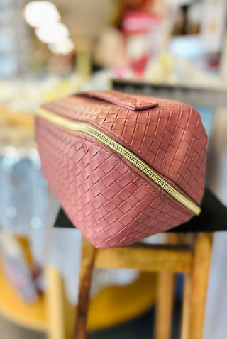 Woven leather makeup bag with gold zipper displayed on blurred retail background