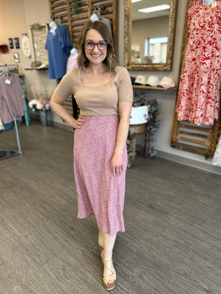 Woman wearing beige ribbed top and floral midi skirt standing in clothing boutique store