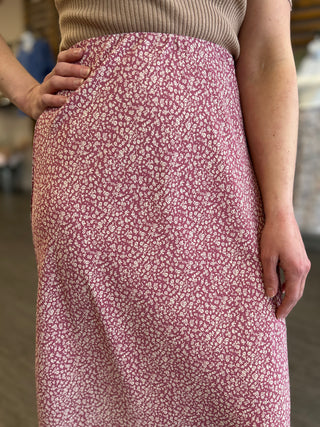 Woman wearing a floral patterned midi skirt with small white flowers on mauve background and ribbed knit top.