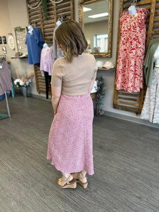 Woman wearing floral midi skirt and beige top in clothing boutique with dress displays