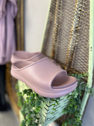Mauve platform slide sandals displayed on decorative mesh surface with greenery and natural lighting