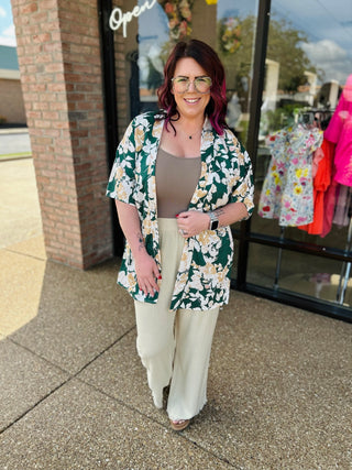 Woman wearing floral kimono over neutral outfit standing outside boutique storefront