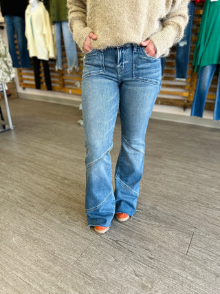 Person wearing medium wash flare jeans with asymmetrical seam details and fuzzy sweater in clothing store.