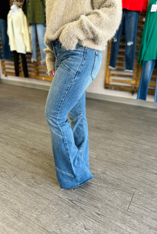 Woman wearing asymmetrical flare jeans with beige sweater, showcasing the unique seam detailing and wide-leg silhouette.