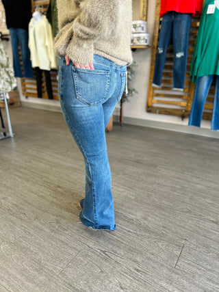 Person wearing medium wash flare jeans with asymmetrical hem and cozy sweater in clothing store