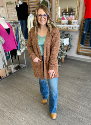Woman wearing medium wash high-rise flare jeans with brown cardigan and mint top in clothing boutique.