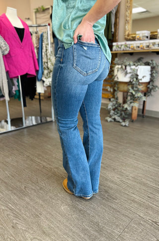 Woman wearing medium wash high-rise flare jeans with mint green top in clothing boutique