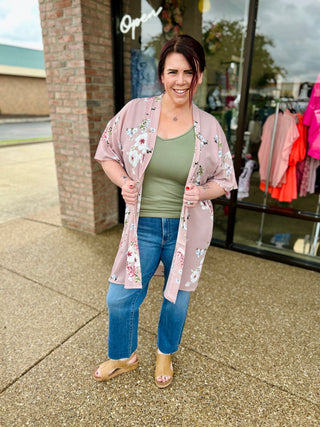 Woman wearing straight-leg denim jeans with raw hem, pink floral cardigan, and green top outside boutique.