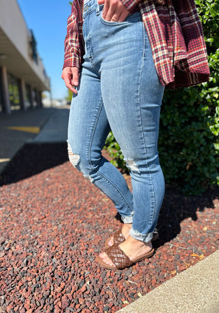 Person wearing distressed skinny jeans with raw hem and ripped knee details, paired with plaid flannel shirt and sandals.