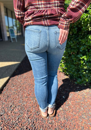 Woman wearing medium wash distressed skinny jeans with raw hem and red plaid flannel shirt.