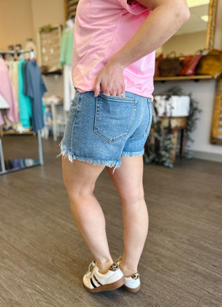 Person wearing medium wash denim shorts with frayed hem and pink top in clothing store