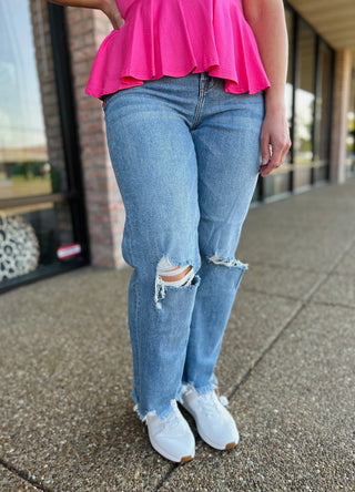 Woman wearing distressed wide leg jeans with frayed hem and bright pink top, standing on sidewalk.